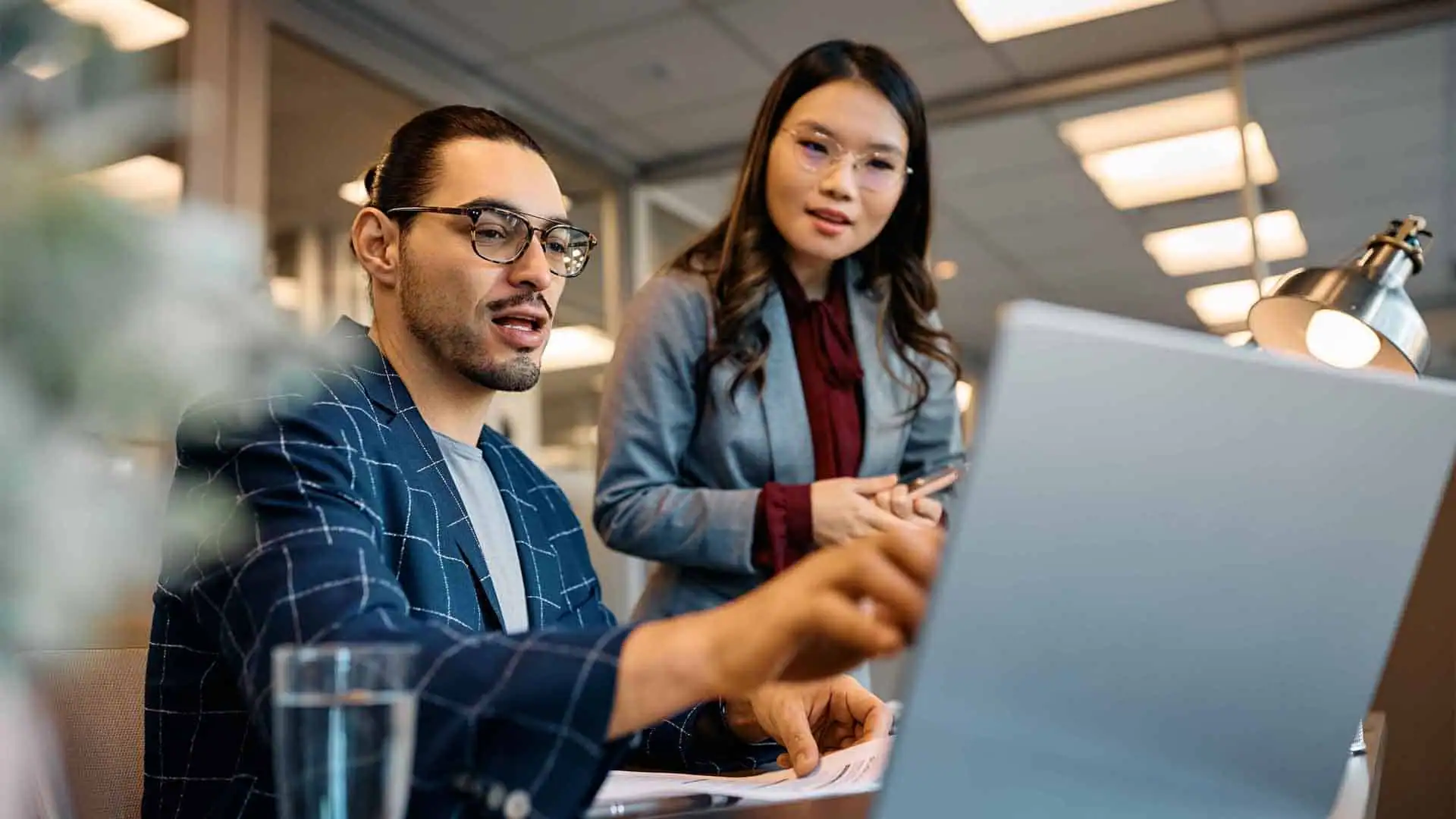A man and a woman in business attire discuss choosing the right ERP solution while looking at a laptop in an office setting.